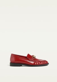 Red leather loafers with a rounded toe, decorative stitching, and gold hardware accent. Flat, durable sole with a smooth finish.