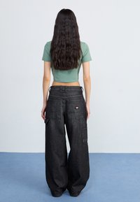 Black wide-leg denim pants with cargo pockets, paired with a short green fitted top. The outfit features a casual, relaxed fit design.