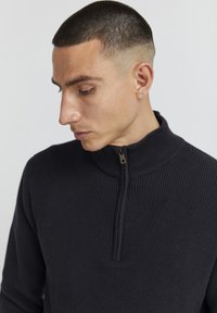 Pulover zip-up de culoare gri închis, cu un guler înalt și un detaliu de fermoar scurt la gât, având un model de tricotat texturat.