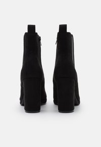 Bottines en daim noir avec un talon épais, fermeture éclair à l'arrière et texture lisse. Design simple et épuré.