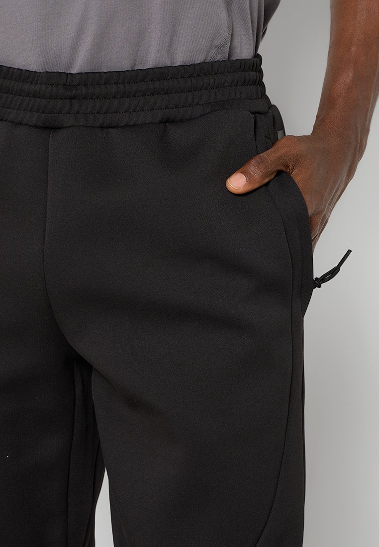 Pantalons de sport noirs avec une texture douce, une taille élastique, des poches latérales et des lignes de design subtiles le long des jambes. Détail à cordon au niveau de la taille.