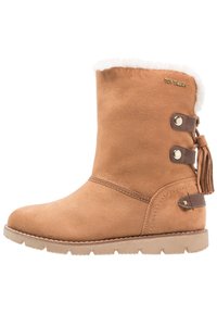 Botte cheville en suède marron avec une douce doublure en fausse fourrure blanche, deux accents marron avec des boutons et un pompon sur le côté, et une semelle en caoutchouc texturé.