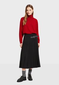 Rode coltrui, zwarte plissé rok met een riem, grijze geribde sokken en zwarte schoenen. Gladde texturen en gestroomlijnd ontwerp.