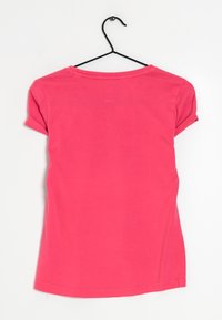 Rosa kortärmad t-shirt med rund halsringning och uppvikt ärm, tillverkad av mjukt bomullstyg, hängande på en svart galge mot en vit bakgrund.