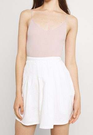 Lichtroze geribbelde body met dunne bandjes gecombineerd met een witte geplooide minirok. De rok heeft een aansluitende tailleband en vallende stof.