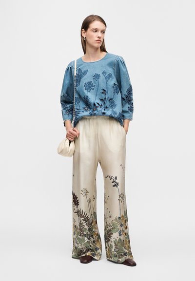 Sweat-shirt en jean avec broderie florale, associé à un pantalon crème à jambes larges orné d'un imprimé floral. Accessoirisé d'un petit sac à main.