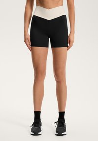 Črne kratke hlače z visokim pasom in bež poudarjenjem na vrhu. Narejene iz raztegljive tkanine, zasnovane za udobje in gibanje.