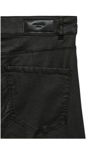 Partie arrière d'un jean en denim noir avec poche plaquée et étiquette de marque en cuir noir cousue sur la ceinture.