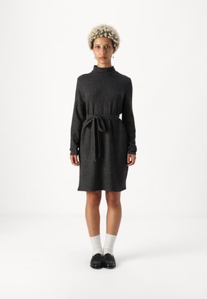 Grå, langermet kjole med høy krage og belte i midjen. Myk tekstur, knelang fasong, brukt med hvite sokker og svarte loafers.