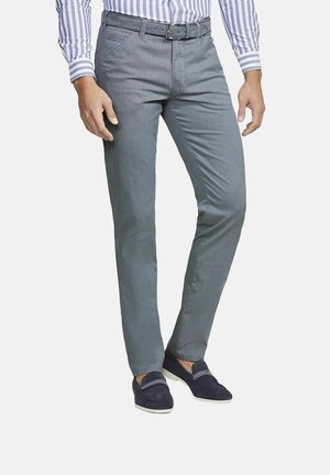 Man wearing slim-fit gray trousers, striped tucked-in shirt, black belt, and navy blue loafers against a white background.