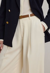 Ναυτικό διπλόφτερο σακάκι με χρυσά κουμπιά, συνδυασμένο με κρεμ παντελόνια. Η καφέ δερμάτινη ζώνη διαθέτει χρυσή αγκράφα με τα αρχικά "RL".