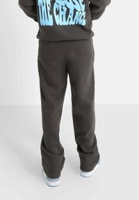 Donkergrijze sweatpants met een relaxte pasvorm, met een gladde textuur en subtiele stiksels, gecombineerd met witte sneakers.