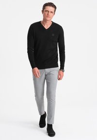Schwarzer V-Ausschnitt-Pullover aus weichem Stoff, kombiniert mit hellgrauen, schmal geschnittenen Hosen. Schwarze Ankle-Boots vervollständigen das Outfit. Einfaches Design und bequeme Passform.