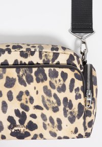 Bolso de estampado de leopardo en beige y negro con forma rectangular, que cuenta con un compartimento con cremallera, herrajes en plata y una correa ajustable.