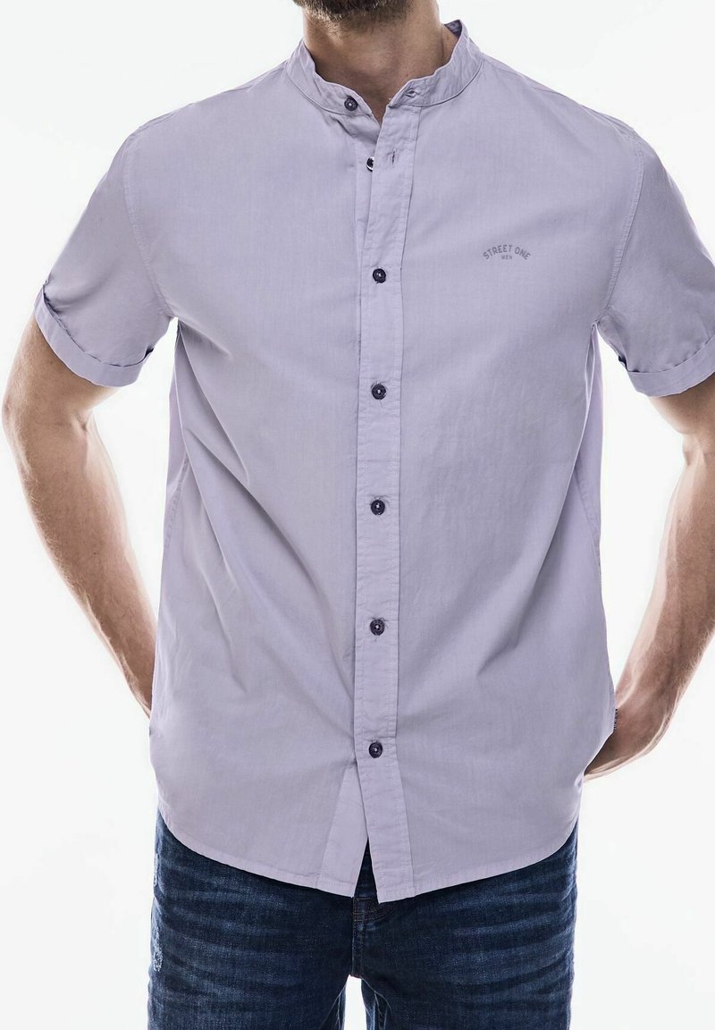 Koszula na krótki rękaw w kolorze lawendowym, z kołnierzykiem mandaryńskim, ciemnymi guzikami i małym logo nadrukowanym na piersi. Gładka tekstura materiału.