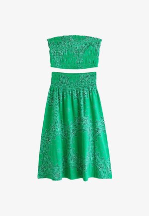 Roheline kaheosaline komplekt koos pitsilise rihmadeta toppi ja kõrge vöökohaga seelikuga, millel on paisley ja lillmustritega kujundus.