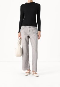 Svart ribbad långärmad topp, ljusgrå vida jeans, vita platta skor och en krämfärgad väska, presenterat mot en enkel bakgrund.