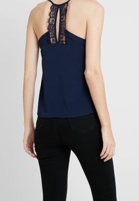 Haut sans manches bleu marine avec des détails en dentelle à l'arrière, encolure arrondie et coupe décontractée, assorti à un jean noir ajusté.