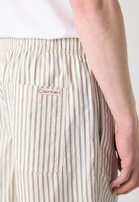 Pantalones cortos a rayas de Calvin Klein en crema y azul marino, con una cintura elástica, bolsillo lateral y una pequeña etiqueta de marca en el bolsillo trasero.