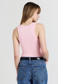 Canotta rosa a costine con scollatura a barca, abbinata a jeans in denim blu a vita alta con una cintura nera e tasche posteriori evidenti.