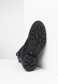 Zwarte leren laars met een gestructureerde rubberen zool, zijrits en reliëflogo. De zool heeft een profielpatroon voor grip.