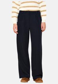 Navy wide-leg pants with pleats, crafted from soft fabric. Features a button closure and side pockets, paired with a striped sweater and brown shoes.