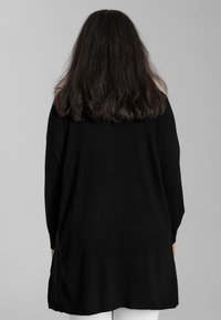 Schwarzes Langarmkleid aus weichem Material, mit lockerer Passform, abgerundetem Saum und minimaler Details.