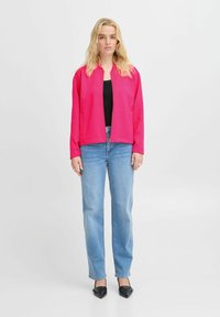 Fuchsiová bunda na zips s stojacím golierom, nosená cez čierny top; skombinovaná so svetlo modrými rovnými džínsami a čiernymi špicatými topánkami.
