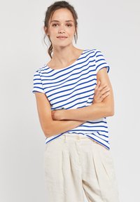 Haut blanc à manches courtes avec des rayures horizontales bleues, encolure ronde et coupe décontractée, associé à un pantalon beige plissé.