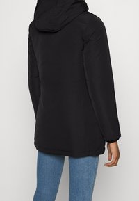 Svart vadderad jacka med huva, med en slät textur och en något oversize passform. Plagget har långa ärmar och rak fåll.