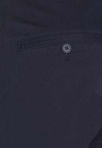 Marina färgade tygbyxor med en slät textur, med en bakficka som är säkrad med en fyrknapps-stängning och en platt söm-detallet.