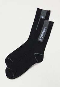 Chaussettes basses noires avec des accents gris sur le poignet, les orteils et le talon, arborant le logo blanc "KOROSHI" verticalement sur le côté.