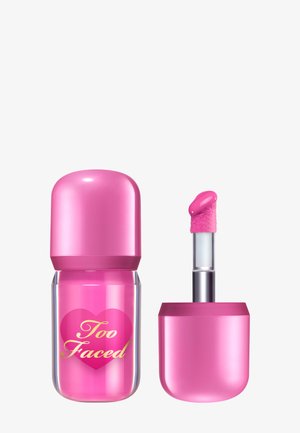 Too Faced lip product in een ronde roze verpakking met een transparante onderkant, voorzien van een zilveren applicator met een zachte roze punt. Gouden logodetail.