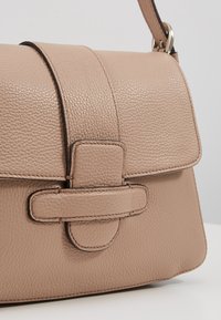 Strukturovaná kabelka z měkké béžové kůže, s texturovaným povrchem, plochým horním zapínáním a plochým popruhem s jemnými švovými detaily.