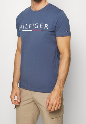 Blå bomuld t-shirt med korte ærmer, rund halsudskæring og en hvid, rød og grå "HILFIGER"-logo tværs over brystet.