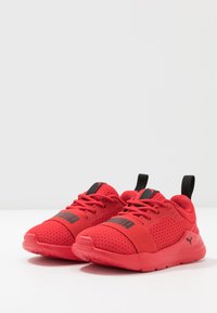 Baskets de sport rouges en maille et matériau synthétique, avec des accents noirs, un bout rond et une semelle arrondie avec une texture adhérente.