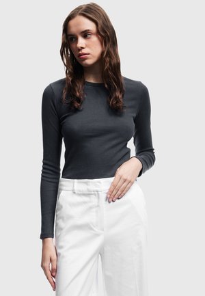 Langsleeve, aansluitend shirt in donkergrijze geribbelde stof, gecombineerd met high-waisted witte broeken. Eenvoudige ronde halslijn en slanke mouwen.