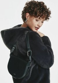 Czarna skórzana torebka crossbody o zakrzywionym, siodłowym kształcie i odczepianym pasku. Torebka ma gładkie wykończenie i subtelny srebrny detal z logo.