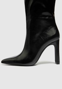 Bota de tacón de aguja negra de cuero con punta afilada, tacón alto, textura suave y detalles de costura mínimos, que exhibe un diseño elegante.