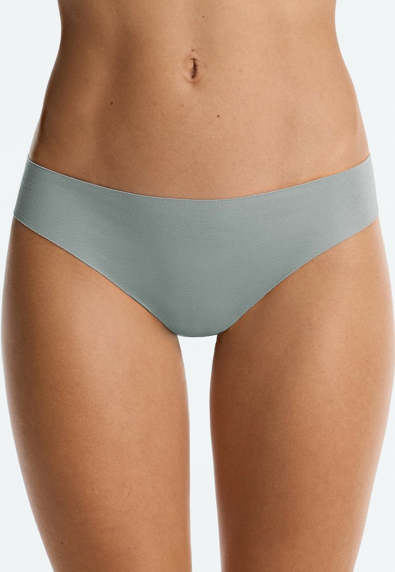 Femme portant des sous-vêtements sans coutures gris clair taille basse montrant le bas-ventre et le haut des cuisses sur fond blanc.