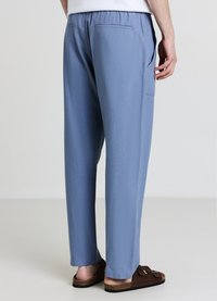 Blaue gewebte Hose mit elastischem Bund, Seitentaschen und einer einzigen Gesäßtasche; glatte Textur mit entspanntem Schnitt.