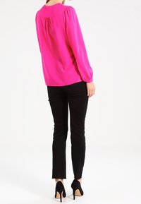 Top fucsia a maniche lunghe con spalle arricciate, indossato con jeans skinny neri e scarpe con tacco nere, visto da dietro.