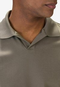 Khaki pikétröja med klassisk krage, korta ärmar och en mjuk textur. Tyget är slätt med minimala synliga sömdetaljer.