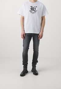 Bílá bavlněná tričko s černým potiskem loga, spárované s tmavě šedými slim-fit džíny a černými kotníkovými botami. Jednoduchý a moderní design.