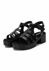 Sandalias de cuero negro con un diseño de punta abierta. Presentan múltiples correas, un cierre de tobillo con hebilla y una suela de plataforma gruesa y texturizada.