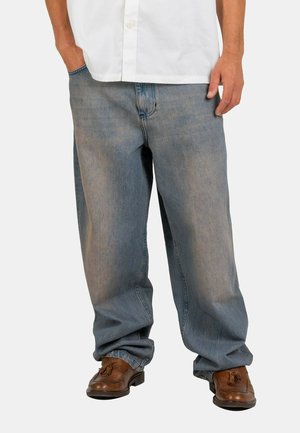 Light blue, loose-fitting denim jeans with subtle faded patches, paired with brown dress shoes. Front pockets and a standard waistband.