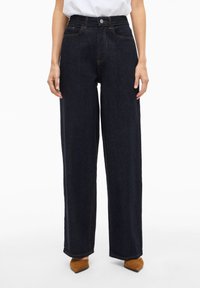 Mørkeblå jeans med vide ben i denimstoff, med høy midje, framlommer og en svak falming. Ferdig med kontrasterende søm.