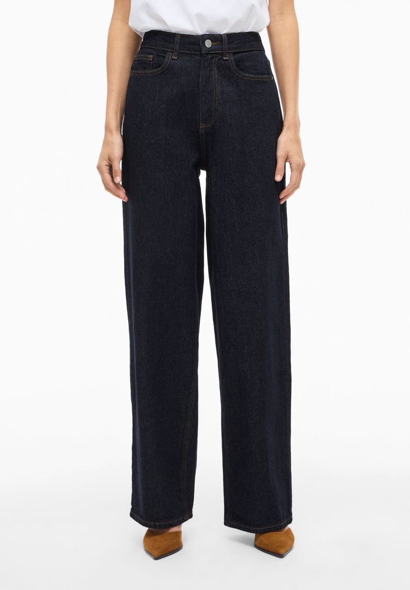 Mørkeblå jeans med vide ben i denimstoff, med høy midje, framlommer og en svak falming. Ferdig med kontrasterende søm.