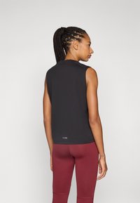 Svart ermeløs topp i et lett stoff, kombinert med maroon tights. Har rund hals og en subtil logo-detalj på baksiden.