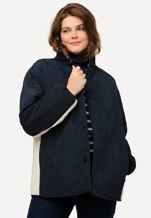 Gepolsterte dunkelblaue Jacke mit einer kontrastierenden cremefarbenen Innenseite, ausgestattet mit einem hohen Kragen, Knopfverschluss und strukturiertem Stoff.
